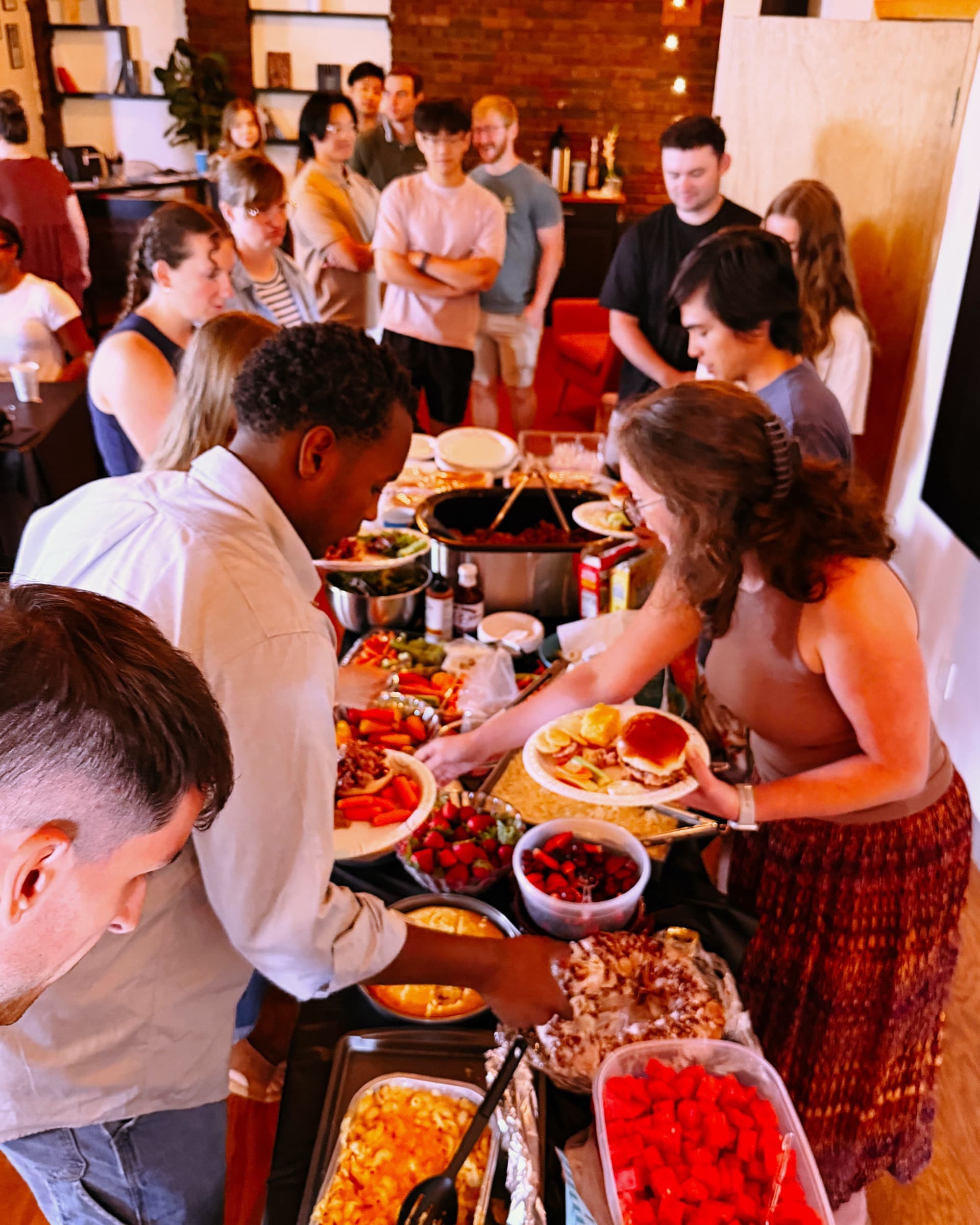 A long potluck table of shared food with the New Culture Church community filling their plates