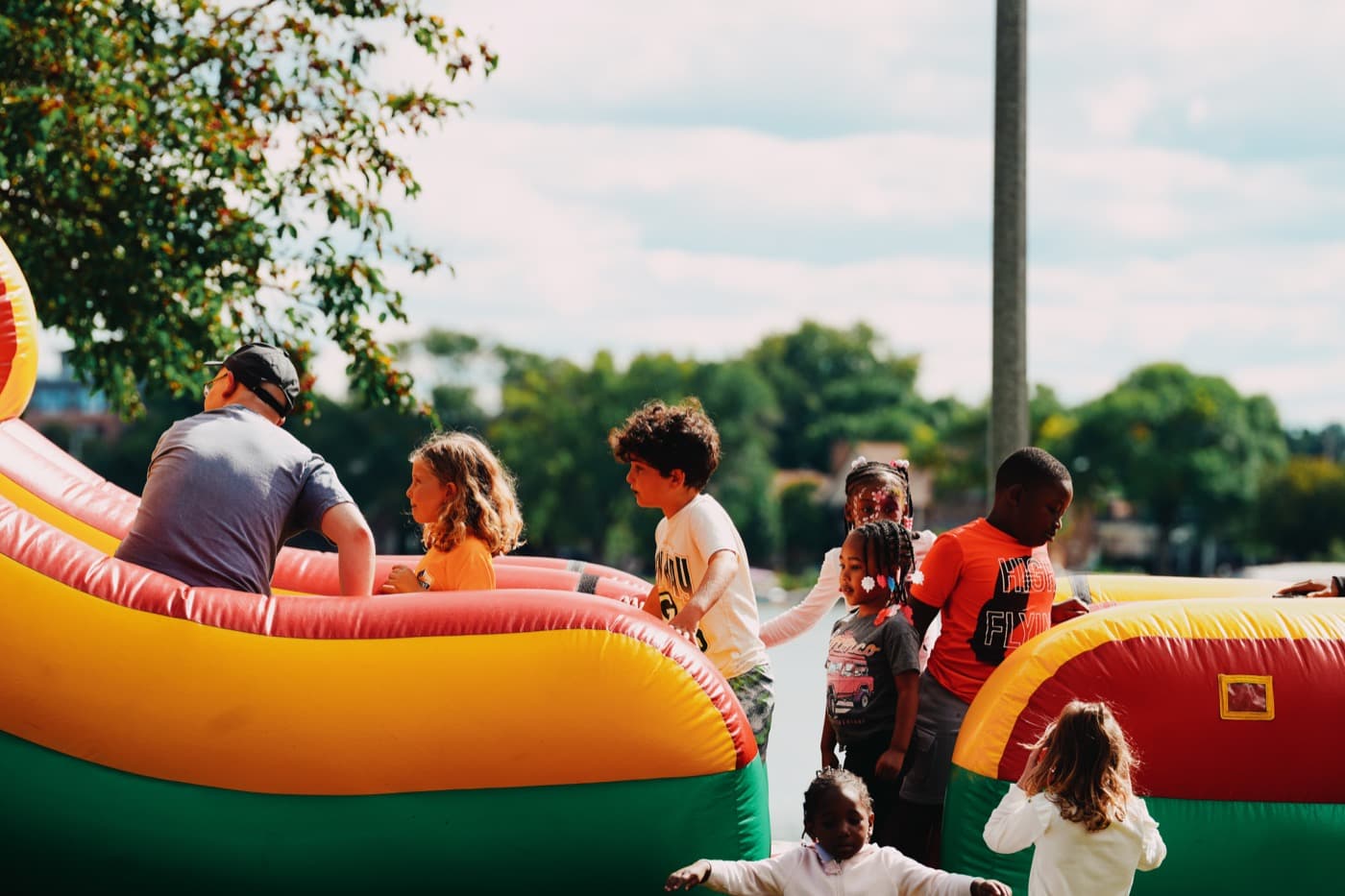 Children climbing on the inflatable obstacle course at the Madison Good Neighbor Gathering, with Monona Bay and the trees behind them