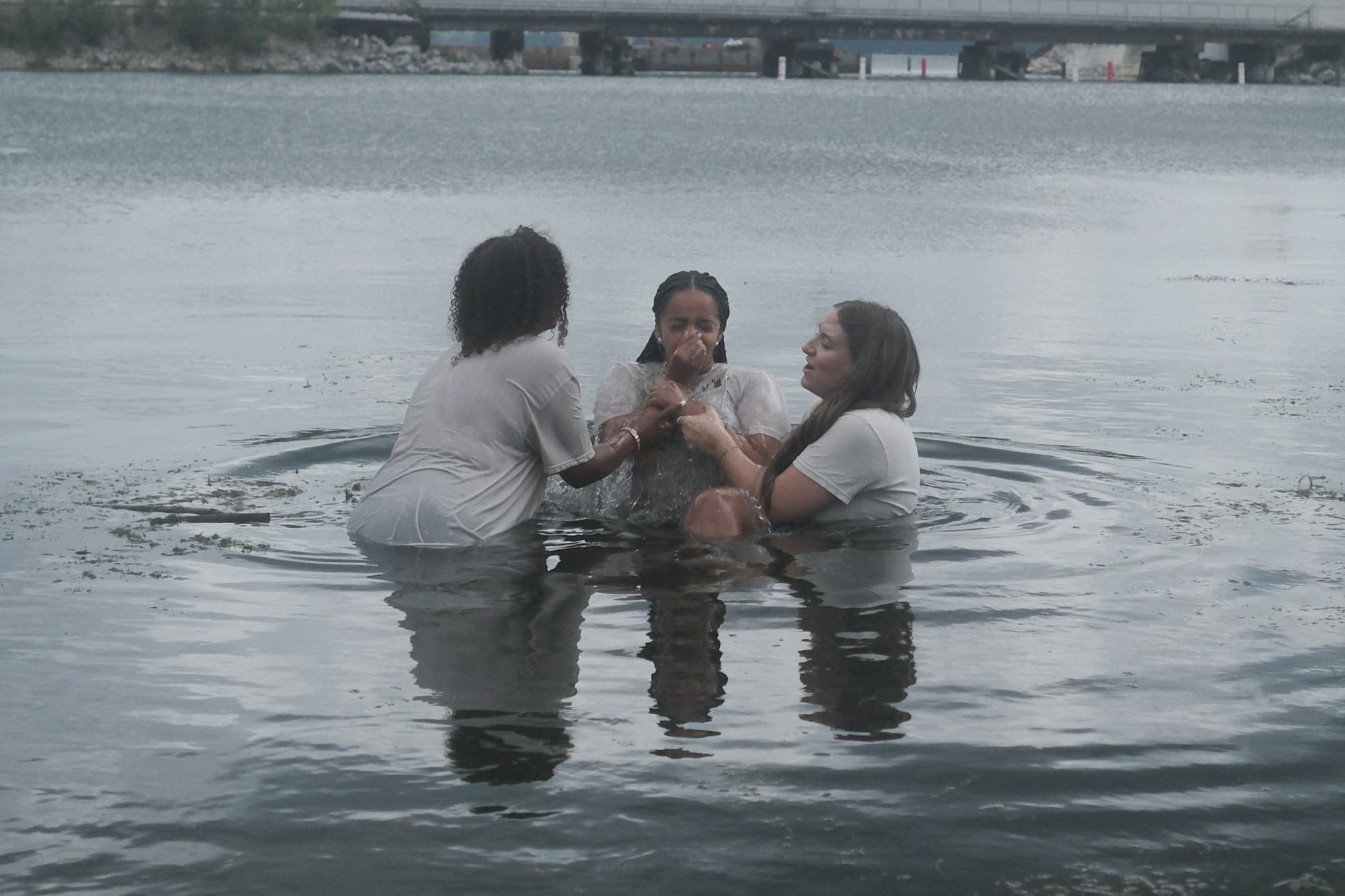A woman being baptized in Monona Bay, lowered into the water by two others from New Culture Church in Madison, Wisconsin