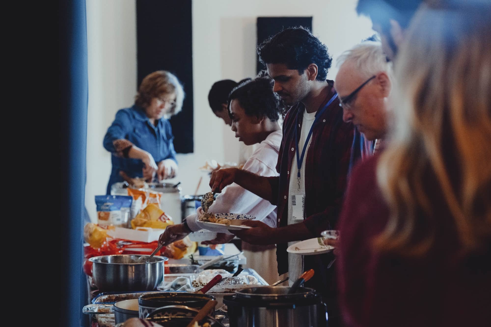People filling their plates along a potluck table at a New Culture Church shared meal in downtown Madison, Wisconsin