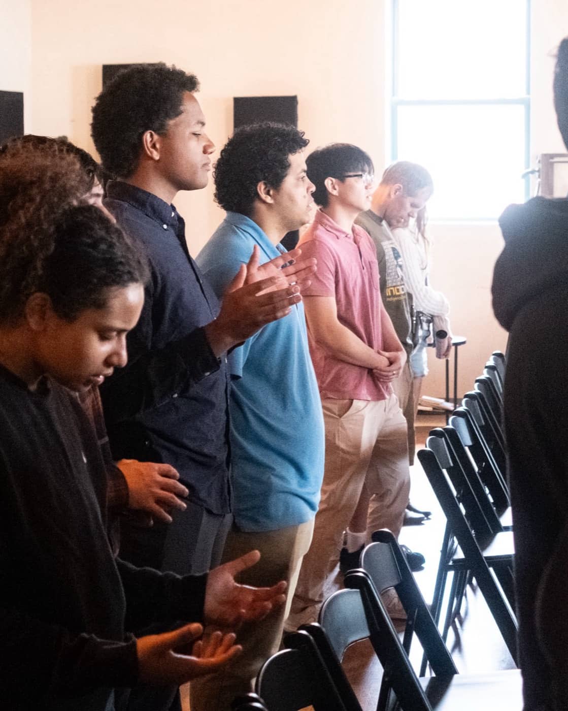 People at New Culture Church standing in prayer with open hands in the sanctuary in downtown Madison, Wisconsin